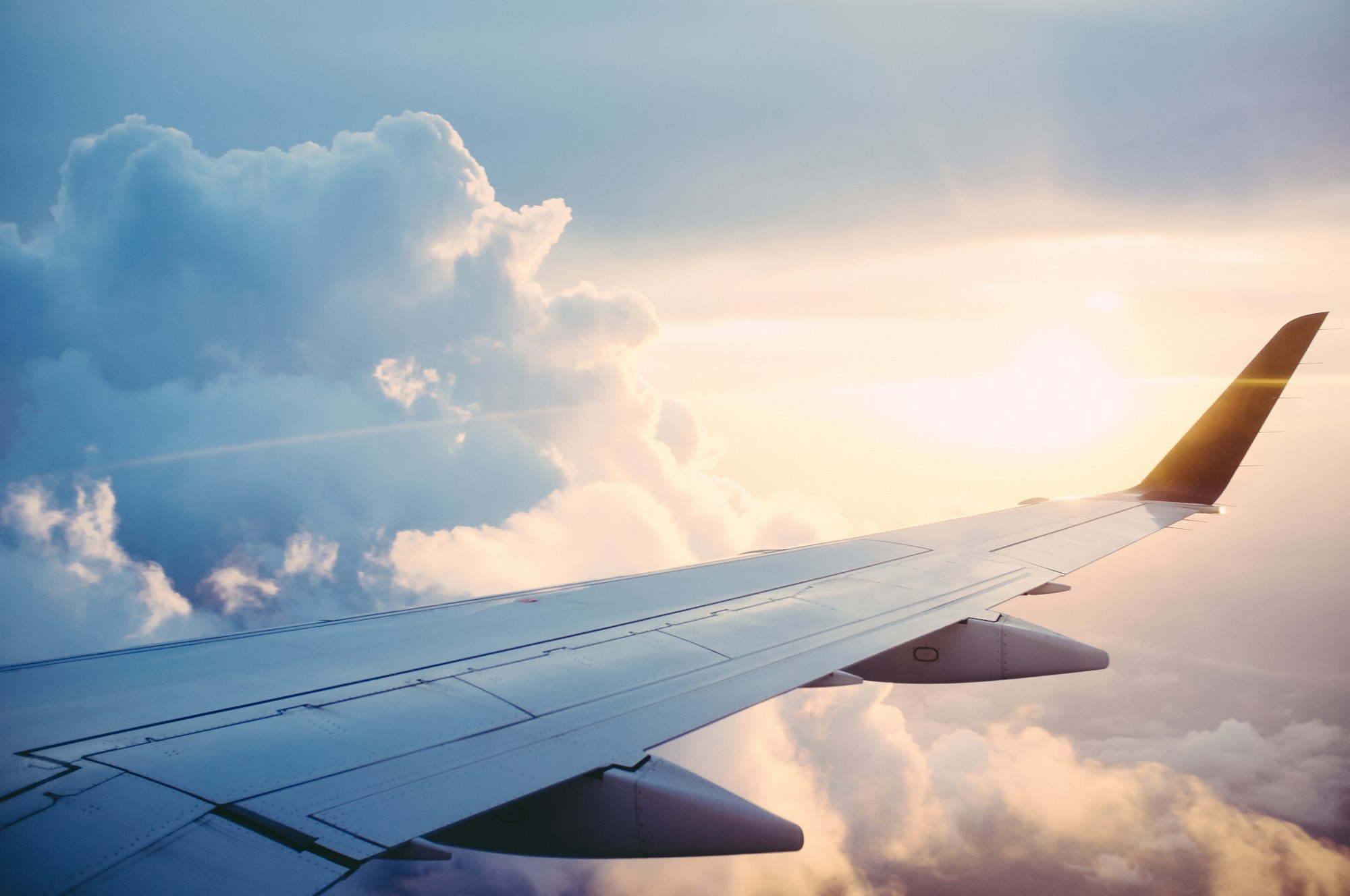 Airplane wing above clouds in a bright sky